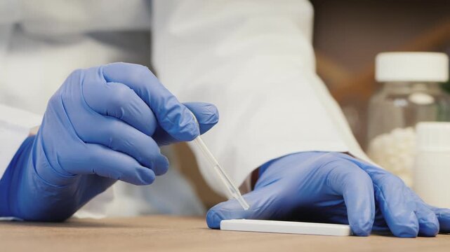 Close up motion of gloved hands in lab coat dropping liquid onto a rapid test device, showcasing medical diagnostic process.