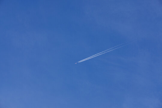Minimalist view of an airplane leaving a white contrail across a clear blue sky.