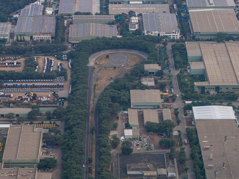 Aerial view of the Mahindra Chakan Plant HUB featuring industrial factory buildings with solar panels, a test track loop, and surrounding greenery in Nighoje, Maharashtra, India.