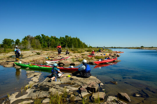 Sea kayakers resting on pink granite shoreline beside beached kayaks on a late morning break, clear blue sky with copy space, Georgian Bay, Ontario