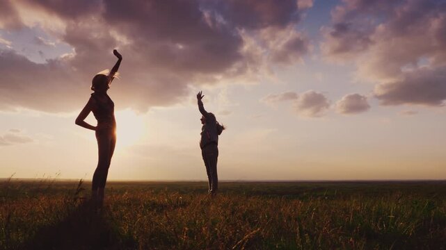 Two women, possibly mother and daughter, silhouettes doing warm-up exercises in a vast field at sunset, dynamic motion footage.