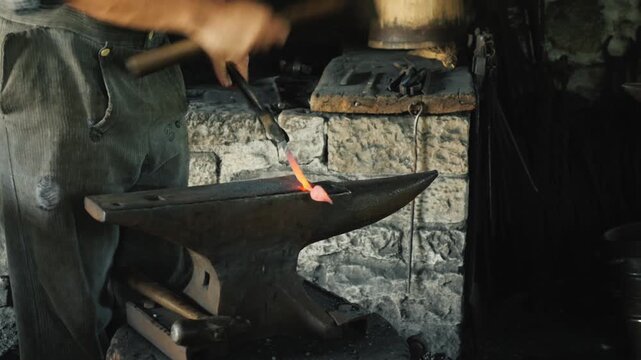 A male blacksmith forging hot metal on an anvil with hammer and tongs, traditional craft in motion.