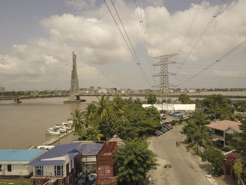Aerial view of the Lekki-Ikoyi Link Bridge spanning the river with power lines, lush trees, and urban buildings in Lekki, Lagos, Nigeria.