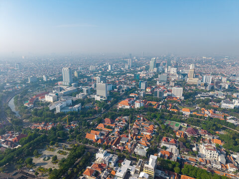 Surabaya, Indonesia - 29 August 2026: Aerial view of the urban landscape, featuring modern high-rise buildings, dense residential neighborhoods with orange-tiled roofs, and lush green spaces.