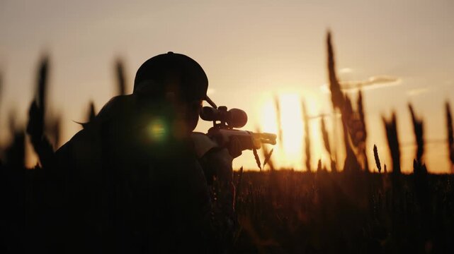 Silhouette of woman aiming with sniper rifle at sunset in wheat field cinematic footage.