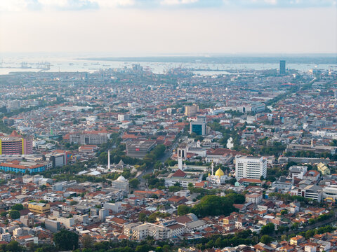 Surabaya, East Java, Indonesia - 28 August 2026: Aerial view of the dense urban landscape, featuring rooftops, mosques with golden domes, and a bustling harbor.