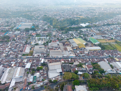 Malang, East Java, Indonesia - 23 August 2026: Aerial view of the city of Malang, showing dense urban housing, industrial buildings, a railway line, and surrounding greenery.