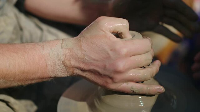 Close up of a skilled potter shaping clay on a spinning wheel, creating a ceramic vase with help of another person in bright sunlight, dynamic motion, artisanal craftsmanship.