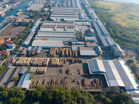 Probolinggo, East Java, Indonesia - 06 August 2026: Aerial view of a large industrial timber processing facility with stacks of lumber, metal-roofed warehouses, and a nearby harbor.