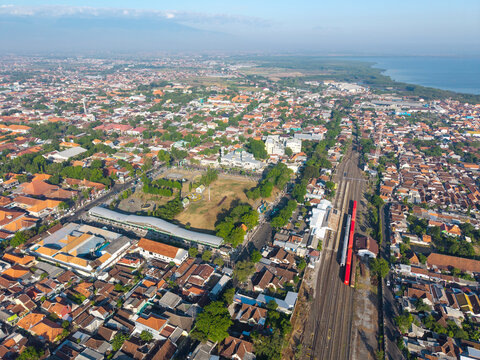 Probolinggo, Indonesia - 06 August 2026: Aerial view of Probolinggo in East Java, showing dense urban rooftops, a central square with a mosque, and railway tracks near the coastline.