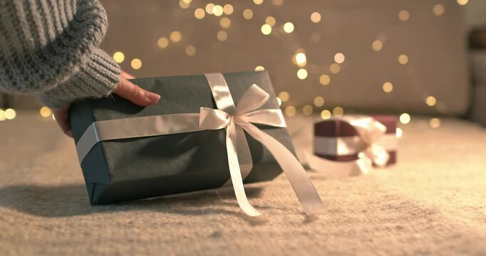 Woman hand taking away green gift box with white satin ribbon on bokeh garland background close up video