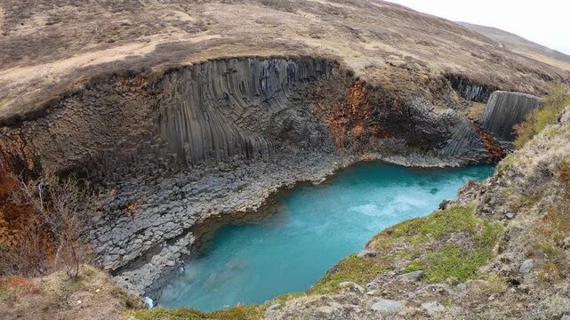 Curving walls of basalt columns above a calm turquoise pool of the glacial river in Studlagil canyon, Iceland.