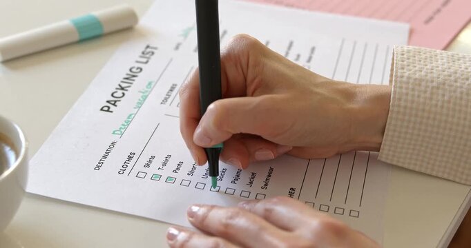 Close up of woman hand writing dream vacation destination with marker on packing list.