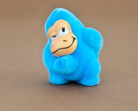 Cute blue flocked gorilla figurine with a funny smirking expression sitting on a brown surface. Ideal for vintage toy, retro, childhood, and humor concepts.