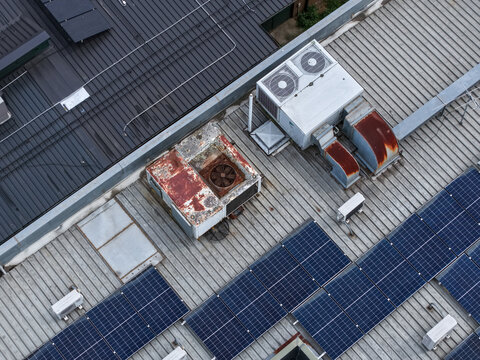 Melbourne, Australia - 25 September 2026: Aerial view of an industrial rooftop featuring weathered HVAC units, rusted ventilation ducts, and rows of solar panels.