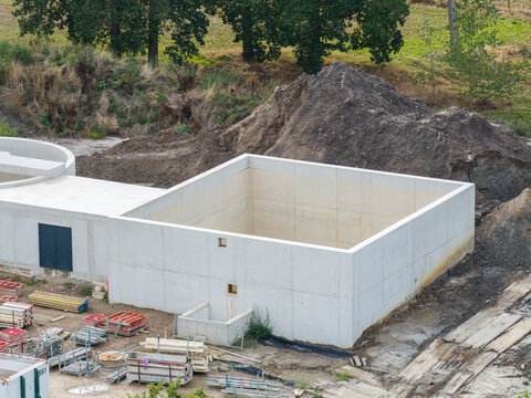 Vilvoorde, Flanders, Belgium - 30 August 2026: Aerial view of a concrete wastewater treatment plant structure under construction with piles of excavated earth and construction materials nearby.