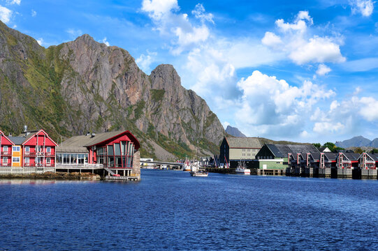 View across Svolvaer harbor in the Lofoten Islands with traditional waterfront houses, steep rocky mountains and blue sky with impressive white clouds.
