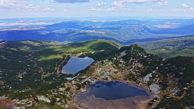 Lush green mountains surround two distinct lakes. The landscape has patches of water and vegetation. The scene shows a clear sky and distant hills.