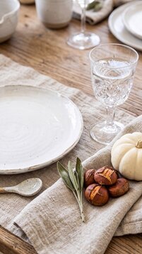 Rustic autumn table setting with empty ceramic plate, crystal glass, roasted chestnuts, white pumpkin and sage on linen napkin