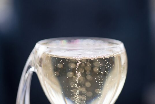 Close-up macro view of golden sparkling champagne with effervescent bubbles rising inside a clear glass against a dark background
