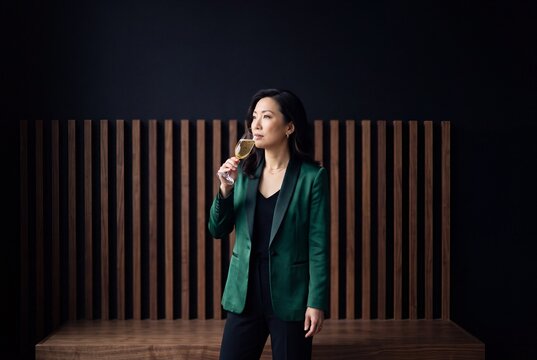 Elegant Asian businesswoman in a green stylish blazer holding and tasting champagne during a luxury corporate celebration event