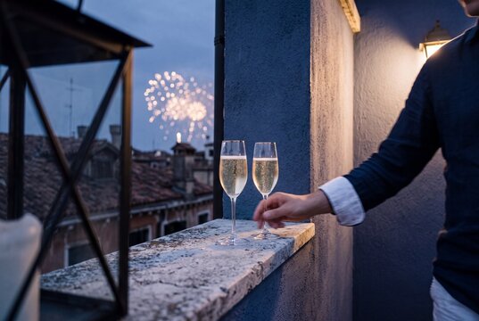 Two glasses of sparkling wine on a rooftop terrace ledge overlooking fireworks in the evening sky during a celebration