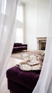Two champagne coupe glasses with white orchids and an ice bucket on a silver tray over a purple velvet ottoman in a luxury room