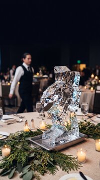 Elegant ice sculpture centerpiece with dripping water on a decorated banquet table during a formal gala dinner with waiter in background