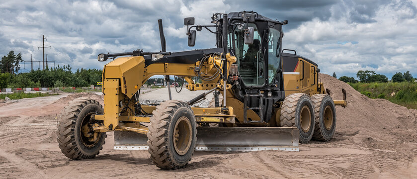 Yellow road grader machine smoothing dirt surface, banner format.