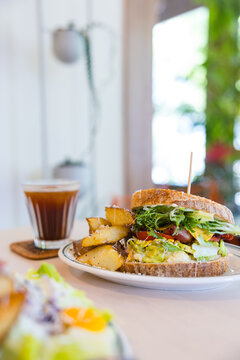 Club sandwich with roasted potato wedges and iced coffee on table&nbsp;