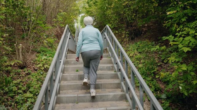 Elderly woman walking upstairs in slow motion, engaging in active lifestyle and fitness on a sunny day in the park.