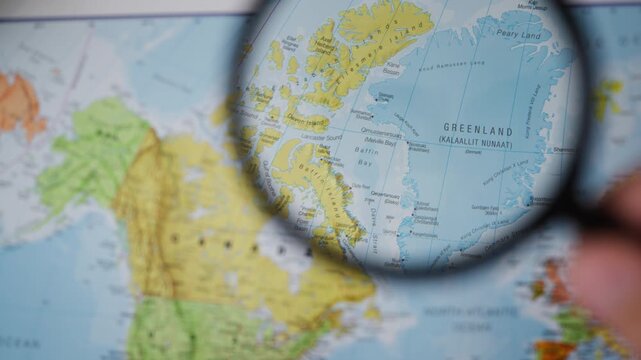 Close-up hand examine Greenland with magnifying glass, symbolizing US interest in acquiring Greenland,Arctic geopolitics,territorial sovereignty,international tensions,strategic competition in Arctic
