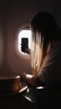 Young woman taking a video on her smartphone of the outside view from the airplane window at golden hour.