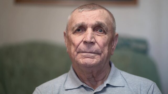 Elderly man portrait, wrinkled face and neutral expression, gray polo, natural indoor light.