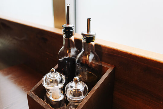 Glass oil and vinegar bottles with salt and pepper mills. Restaurant table condiment set in wooden holder. Clear glass containers background. Dining table accessories. Classic food service equipment.