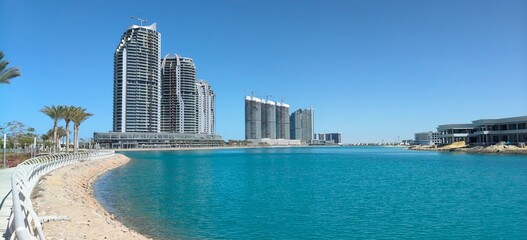 Modern skyscrapers and a scenic promenade along the turquoise lagoon in the coastal city of New Alamein, Egypt, under a clear blue sky. © Mahmoud Asaad