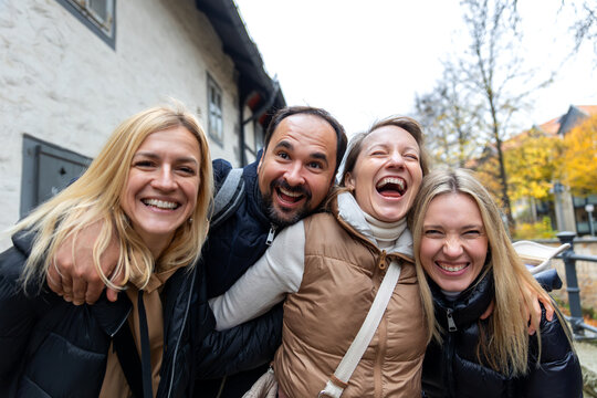 Cheerful friends laugh together on autumn city walk, sharing hugs and joyful travel moments. Candid group portrait captures friendship, reunion, happiness, leisure and weekend adventure outdoors