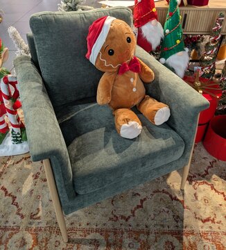 Mu&ntilde;eco de peluche de hombre de pan de jengibre, con sombrero de Santa Claus, sentado en un sill&oacute;n junto a decoraci&oacute;n de Navidad 