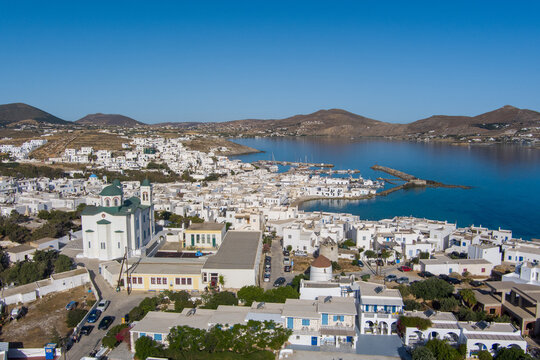 Parikia, Greece - 21 September 2026: Aerial view of the coastal town of Parikia on Paros, featuring white-washed buildings, a church with a green dome, a harbor, and blue waters.