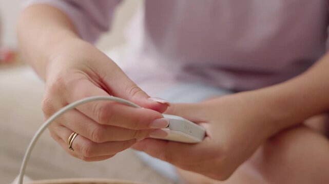 Woman hands holding power bank and plugging in charger cable on comfortable bed close up.