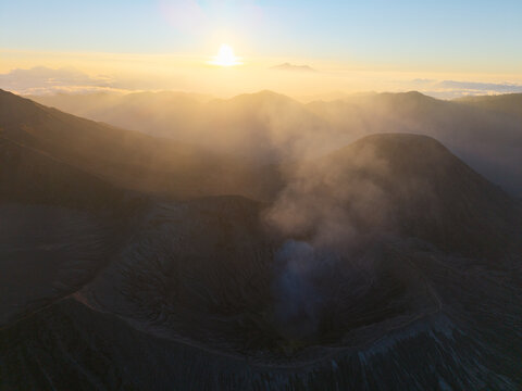 Aerial view of Mount Bromo crater with volcanic smoke rising under a golden sunrise in Tosari, East Java, Indonesia.