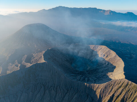 Aerial view of Mount Bromo crater with volcanic smoke rising from the rugged landscape in Tosari, East Java, Indonesia.