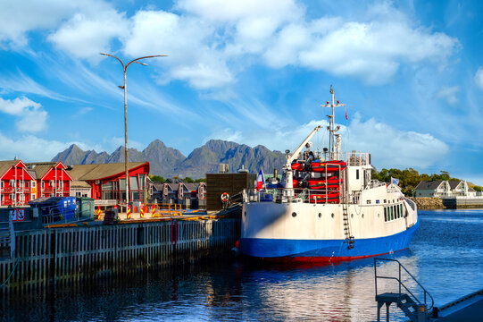 Ship moored in Svolvaer harbor in the Lofoten Islands, with colorful houses and distinctive mountain scenery beneath a clear blue sky.