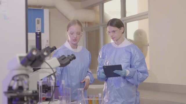 Two lab technicians work together in a modern laboratory with microscopes and samples during a research session