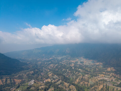 Aerial view of the lush green mountainous landscape of Wonokerto with dense vegetation and clouds over the peaks in Sukorejo, East Java, Indonesia.