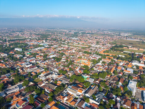 Aerial view of the urban landscape featuring dense residential rooftops, scattered green trees, and local infrastructure in Probolinggo, East Java, Indonesia.