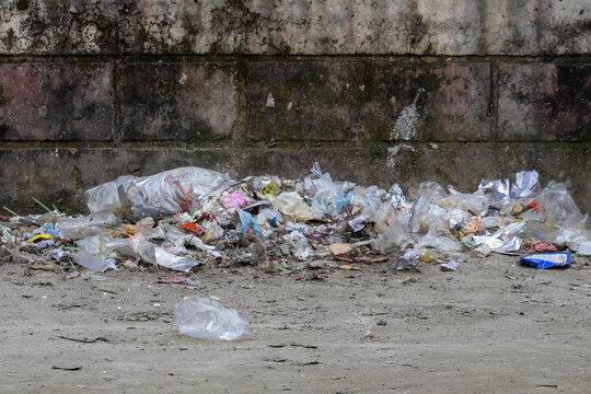 Pile of plastic waste trash and garbage dumped on ground along dirty concrete wall outdoors.