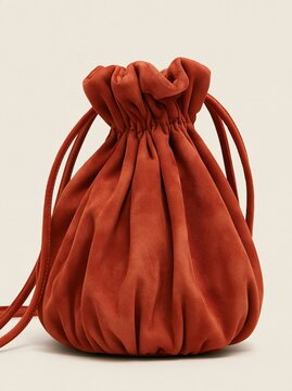 Gorgeous warm terracotta orange suede leather drawstring bucket crossbody bag displayed on neutral beige background minimalist fashion product photography