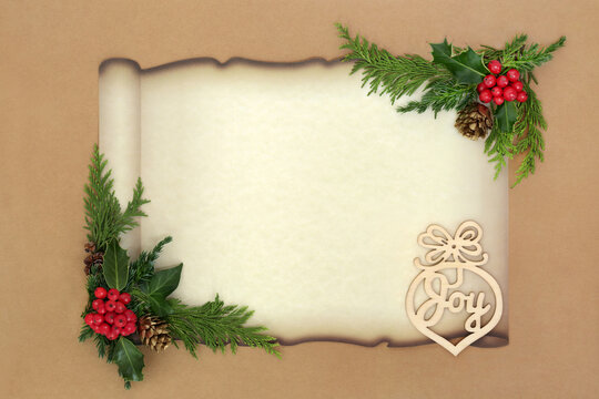 Glad tidings of joy concept Christmas winter flora border on paper scroll with wooden sign, holly, fir, pine cones on brown paper background.  