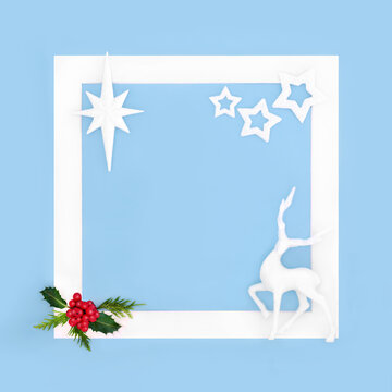 Christmas reindeer, winter holly berry and star decorations border white frame, on pastel blue background. North pole cold concept for greeting card. 